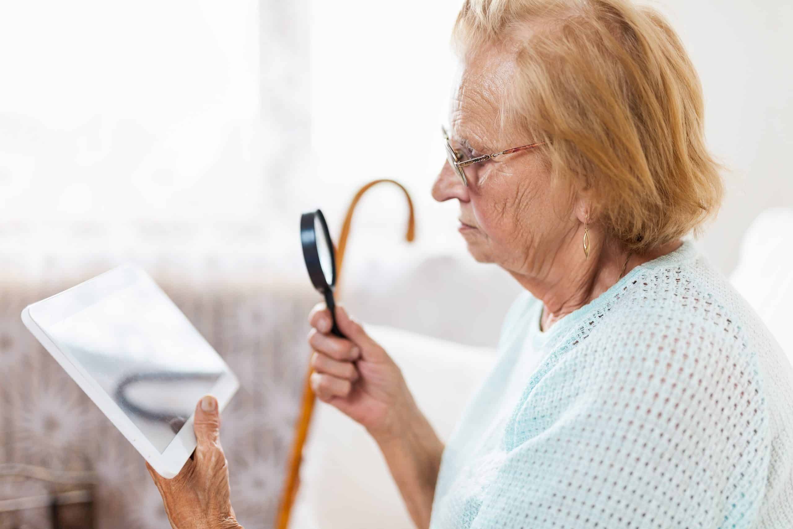 Elderly woman with glasses and loupe using a modern digital tablet