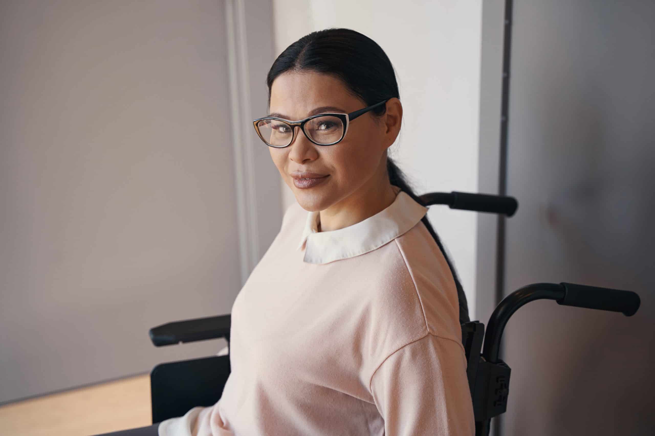 Waist up portrait of smiling bespectacled female who is using wheelchair during day at home