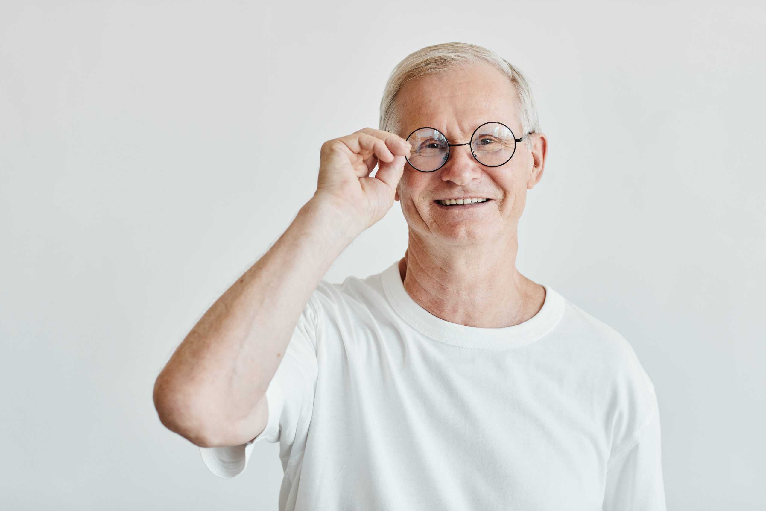 Waist up portrait of smiling senior man wearing glasses while standing against white background, copy space
